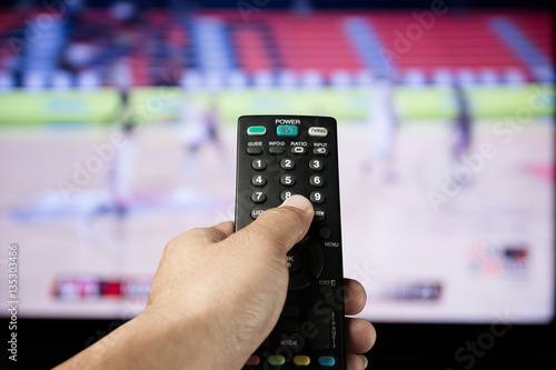 Hand of man holding remote control TV on sport channel program