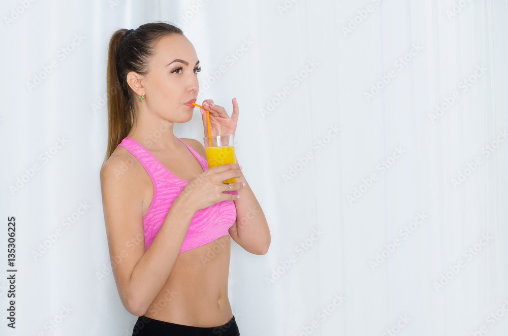 Beautiful girl in sportswear drinking fresh juice through a straw from a glass. On a white background Beautiful girl in sportswear drinking fresh juice through a straw from a glass. On a white background