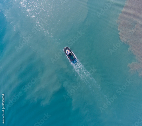 Top view of motion tugboat at azure water with a spot of oil. © chocolatefather