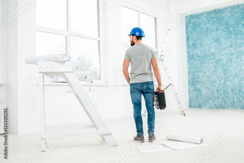 Foreman or worker in uniform with instruments standing back in the white interior during the renovation