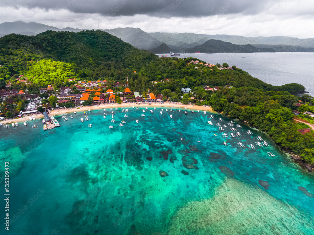 Aerial shot of the tropical bay with sandy beach, boats and buildings. Village of Padang Bai, Bali, Indonesia