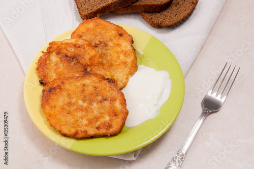 Potato pancakes with meat and sour cream on green plate with rye