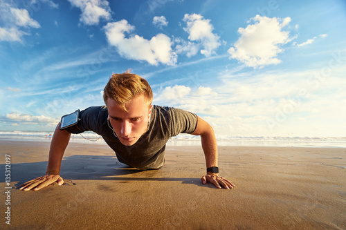 Sports and healthy lifestyle. Young man doing push-ups on the ocean beach.