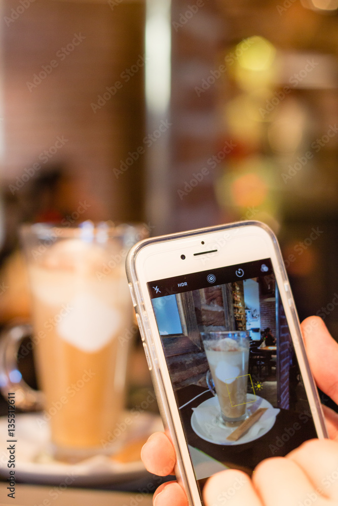 Taking picture of latte coffee with smartphone in cafe