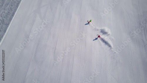 4k footage, top aerial drone view two skiers skiing on empty ski slope in clouds of snow
