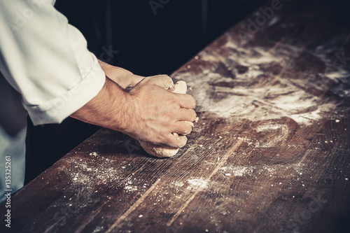 Professional chef kneads the dough for pizza on a wooden table. Flour around. Only hands, close up