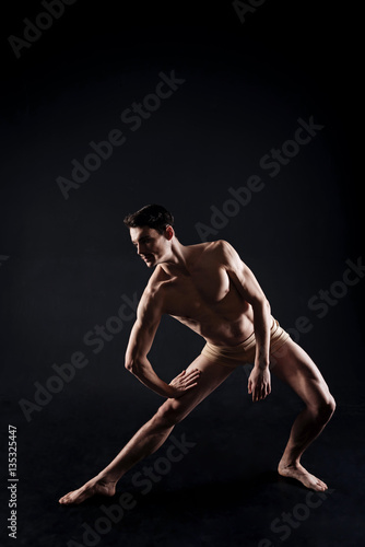 Involved young athlete stretching in the black colored studio