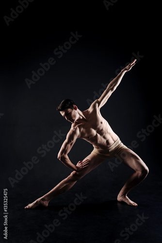 Muscular young athlete stretching in the black studio