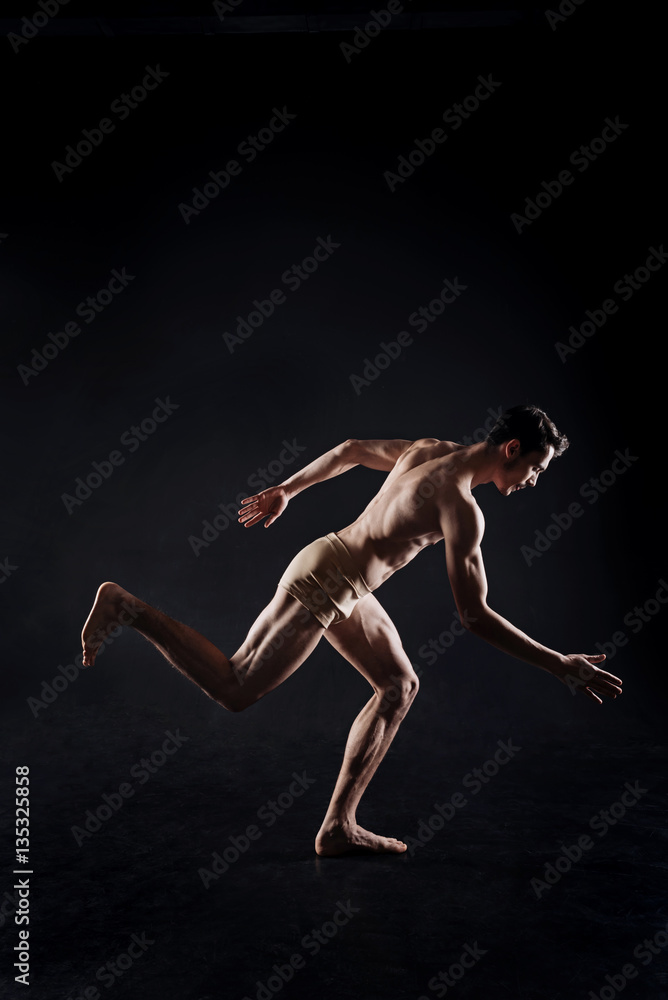 Muscular athlete posing in the dark lighted studio