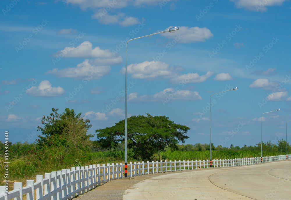 Concrete road with white fence and street lamp in day blue sky background.