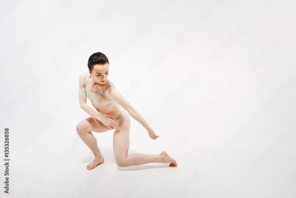 Concentrated young gymnast dancing in the white colored studio