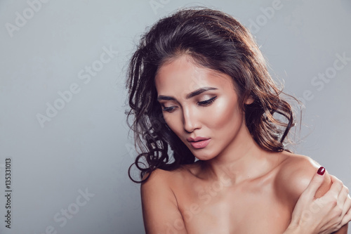 Brunette girl with shiny wavy hair and beautiful make up posing at studio on grey background.