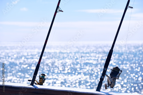 fishing rods with reels spinning on a background of sparkling in the sunlight sea surface. 
