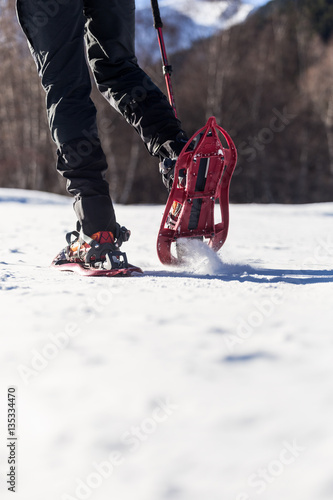 Young man walking in snowshoes over winter background.