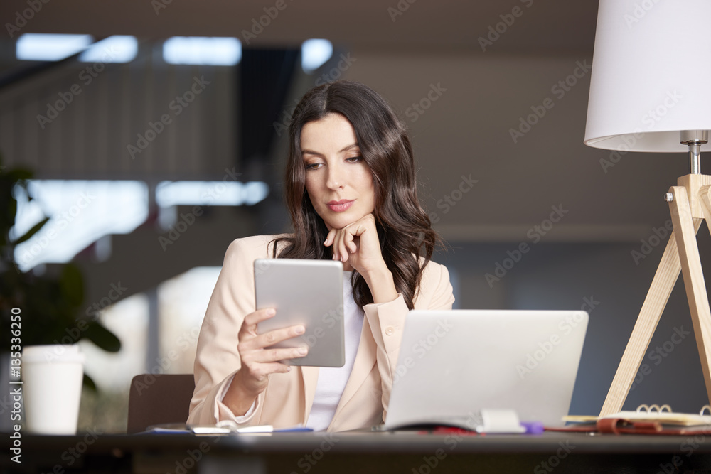 Exploring modern technology. Shot of a confident professional female using digital tablet while sitting at office in front of computer. Exploring modern technology. Shot of a confident professional female using digital tablet while sitting at office in front of computer.