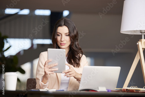 Exploring modern technology. Shot of a confident professional female using digital tablet while sitting at office in front of computer.