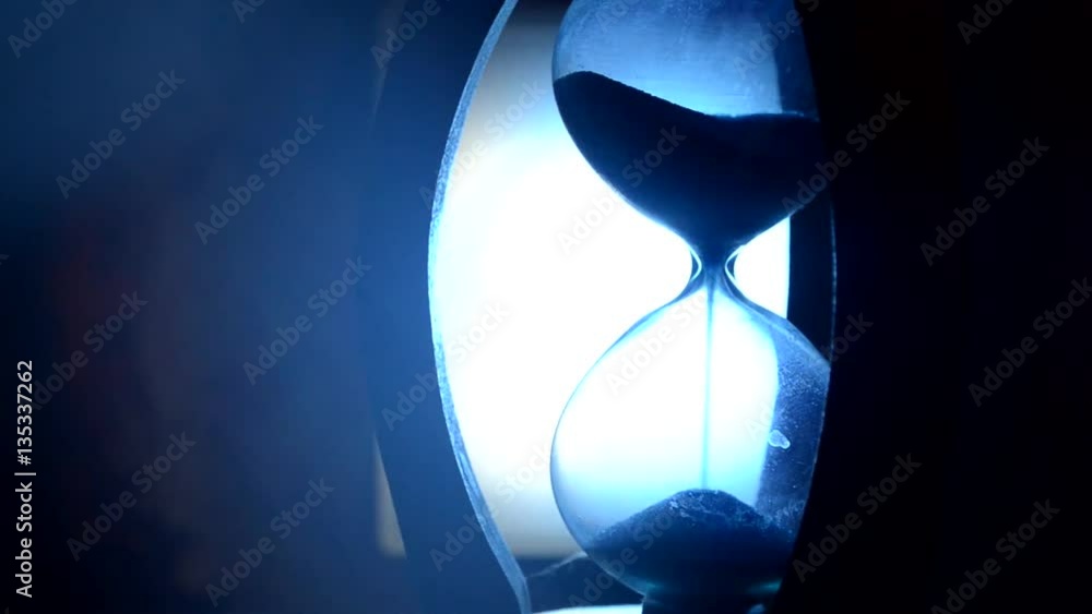 ime concept. Silhouette of Hourglass clock and old vintage wood clock with arrow and smoke on dark background with hot yellow orange blue cold back lighting, or symbols of time under smoke, the end