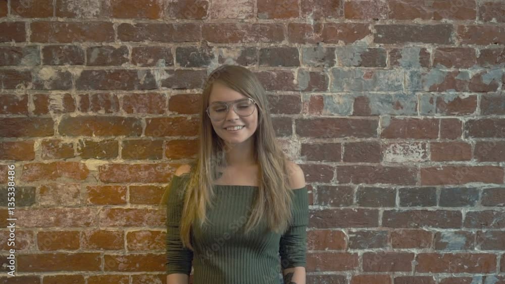 Beautiful young girl with tattoo is looking at camera and smiling while standing against red brick wall Beautiful young girl with tattoo is looking at camera and smiling while standing against red brick wall
