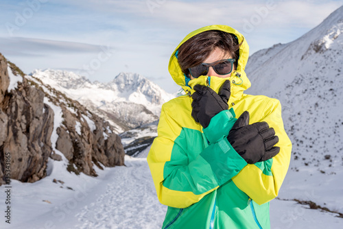 Woman feeling cold discomfort covering her mouth and face from the wind wearing gloves, hood, glasses and windstopper, at extreme snow elements environment on a snowy mountain with low temperature. photo