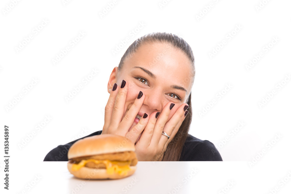 Young girl looking at cheeseburger in excitement, girl and burger in white plate over table, isolated on white background. Young girl looking at cheeseburger in excitement, girl and burger in white plate over table, isolated on white background.