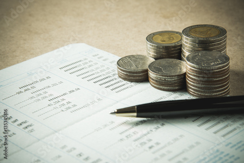 row of coins and pen on account book in finance and banking conc