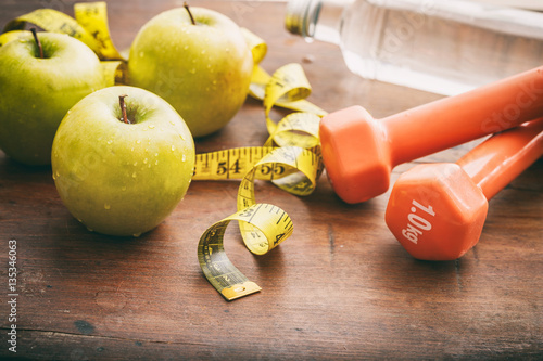 Fitness concept. Green apples, dumbbells and measuring tape on wooden background