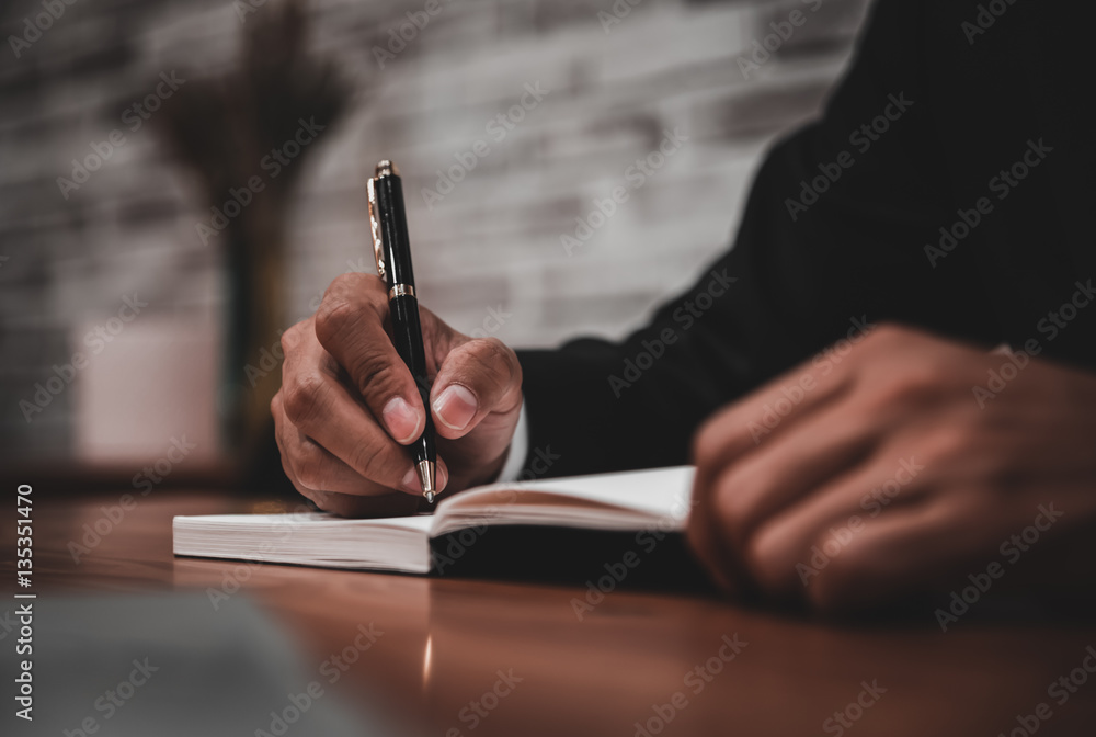 Businessman in suit writing or signing in notebook on wooden tab Businessman in suit writing or signing in notebook on wooden tab