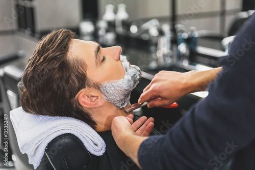 Skillful hairdresser using blade for shaving beard