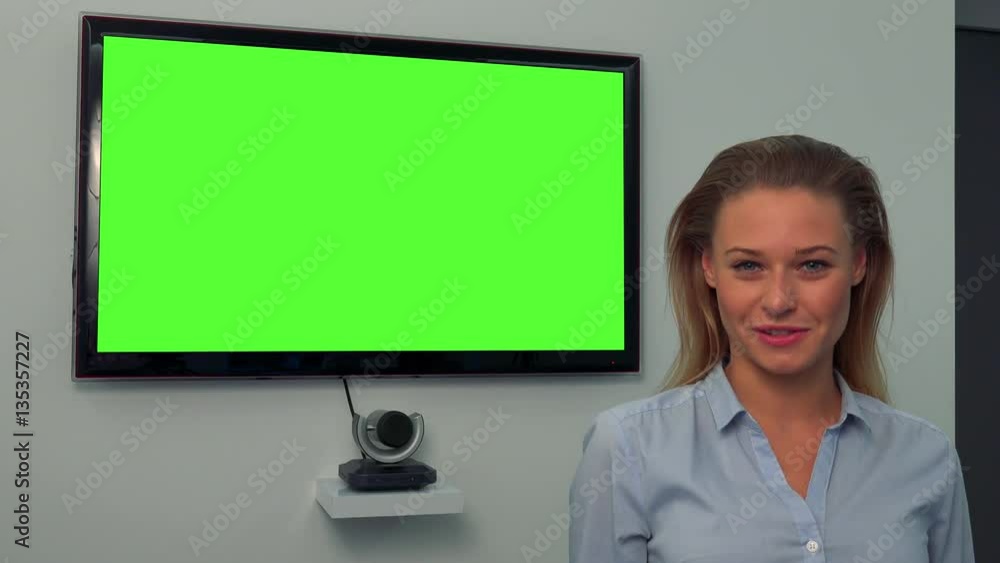 A young, beautiful woman talks to the camera, a green television screen in the background A young, beautiful woman talks to the camera, a green television screen in the background