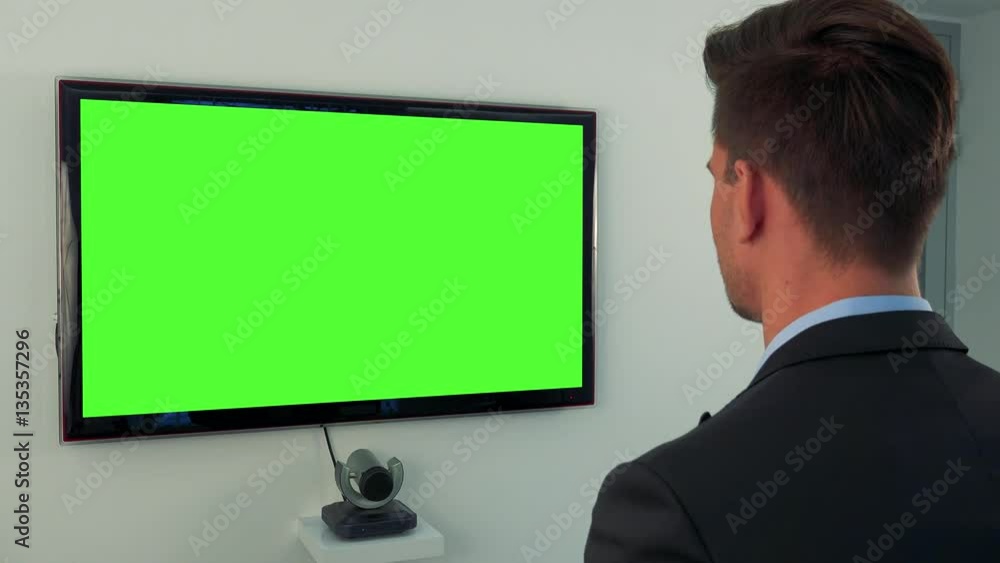 A man in a suit looks at a green television screen A man in a suit looks at a green television screen