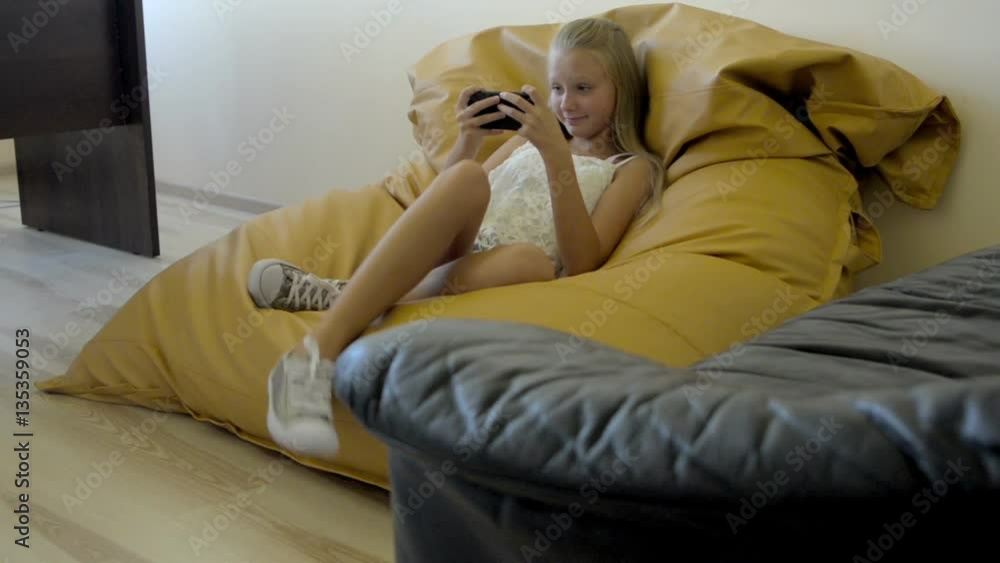 Teenager girl sitting on armchair and playing with cellphone Teenager girl sitting on armchair and playing with cellphone