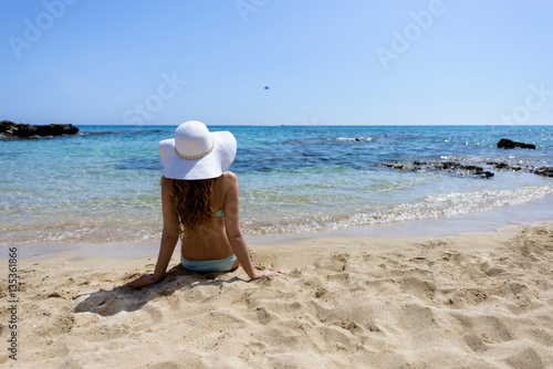 Young woman sitting on the beach. Portrait of a girl in white hat relaxing at...