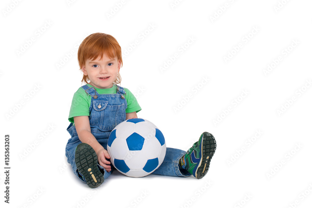 the little child with red-hair sits with a soccerball