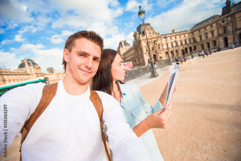 Happy young couple with map of city taking selfie in Paris outdoors