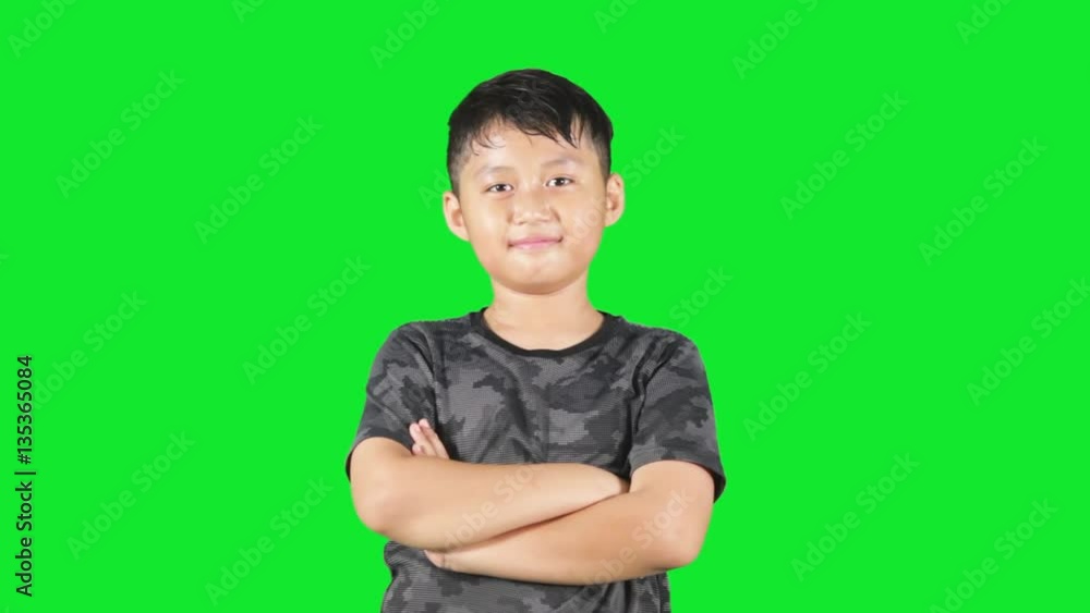Little boy standing in the studio in front of a green background while folded hands and showing thumbs up Little boy standing in the studio in front of a green background while folded hands and showing thumbs up
