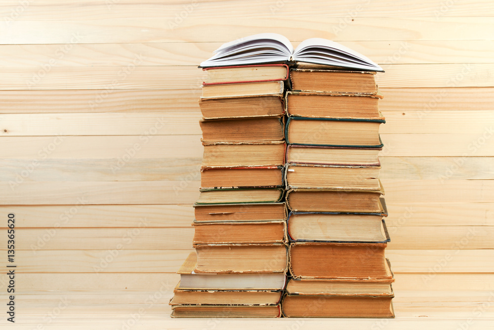 Fototapeta premium Open book, stack of hardback books on wooden table.