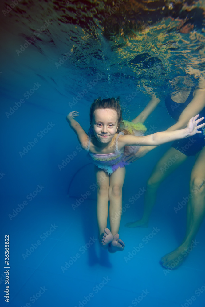 The little girl dives under water surrounded by bubbles, and mom helps her. Portrait. Shooting under the water surface. Vertical orientation