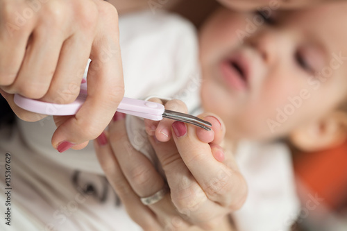 Mother cutting fingernails of her nine months old baby girl
