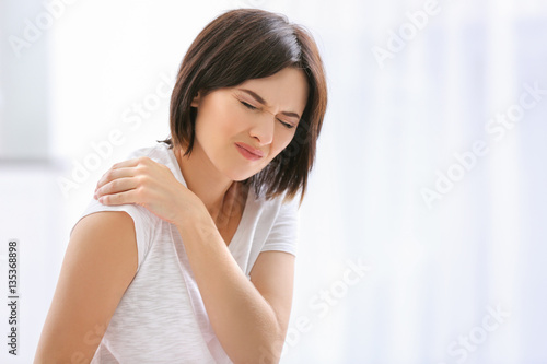 Beautiful young woman suffering from pain in shoulder at home photo