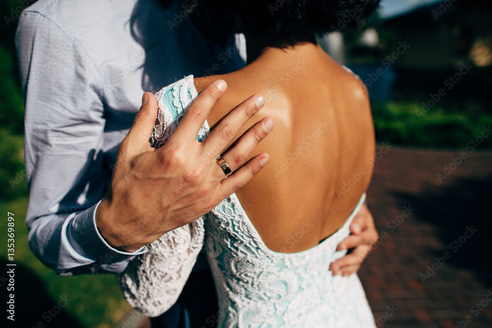 Hand of groom with wedding ring embracing shoulder of bride