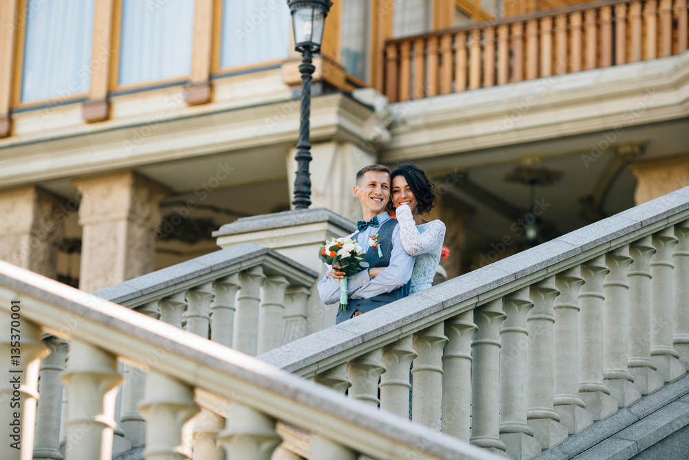 Happy bride and groom hugging on stairs of mansion