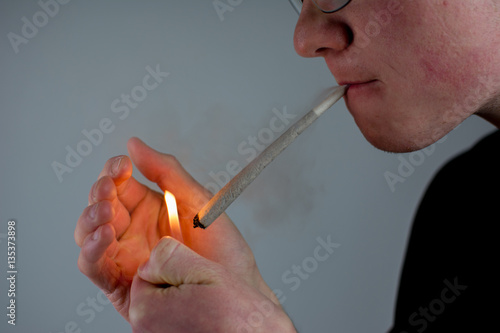 Mann hält einen Joint in der Hand und zündet ihn mit dem Feuerzeug an photo