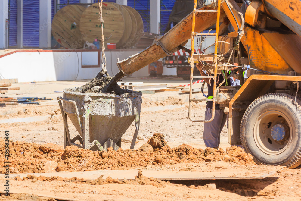 Fototapeta premium Concrete mixer truck pouring liquid concrete into the tower crane bucket at the construction site, Close up