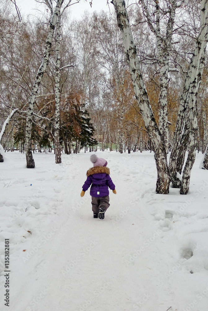 Child in lilac winter clothes walking in winter park