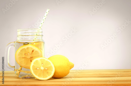  Citrus lemonade water with lemon sliced , healthy and detox water drink in summer on wooden table . vintage color tone