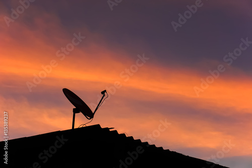 Skyscape in evening with silhouette roof and  satellite dish.