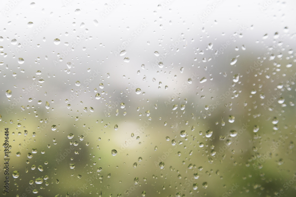 Rain water droplets on glass window with scenic greenery view