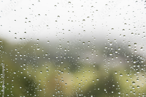 Rain water droplets on glass window with scenic greenery view