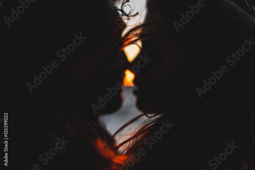 Young hipster couple with long curly hair kissing at sunset
