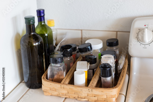 Green glass bottle with olive oil, jars of spices, salt and peper on a tray in the kitchen near the stove